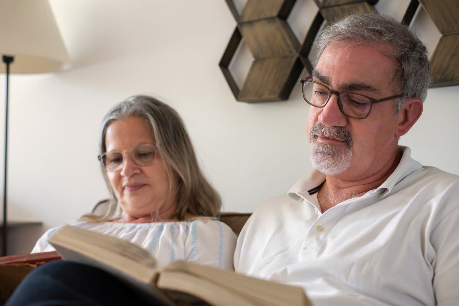 Un couple de retraités lit un livre ensemble, assis dans son salon.
