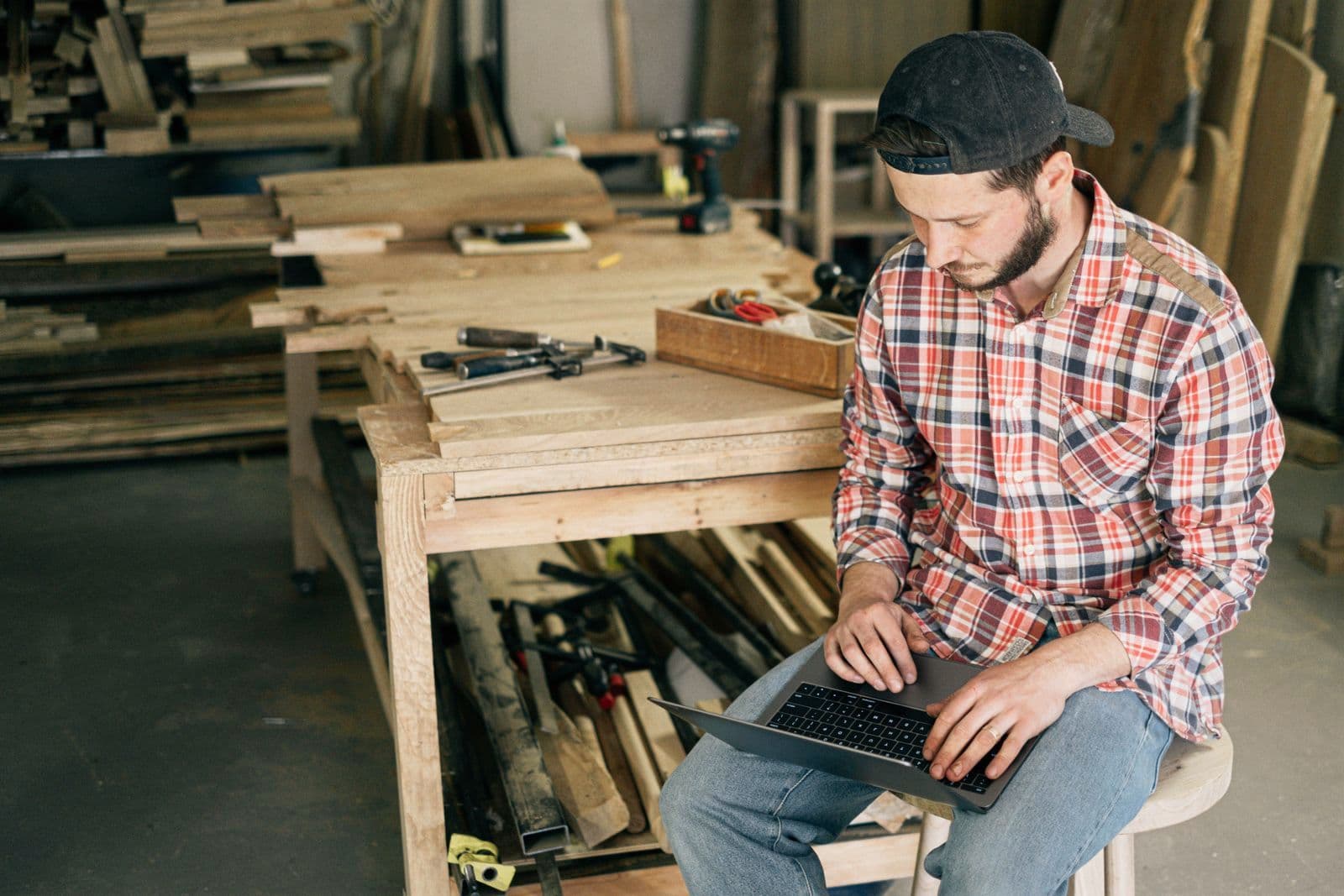 Un dirigeant travaille sur son ordinateur portable, assis dans son atelier de menuiserie.