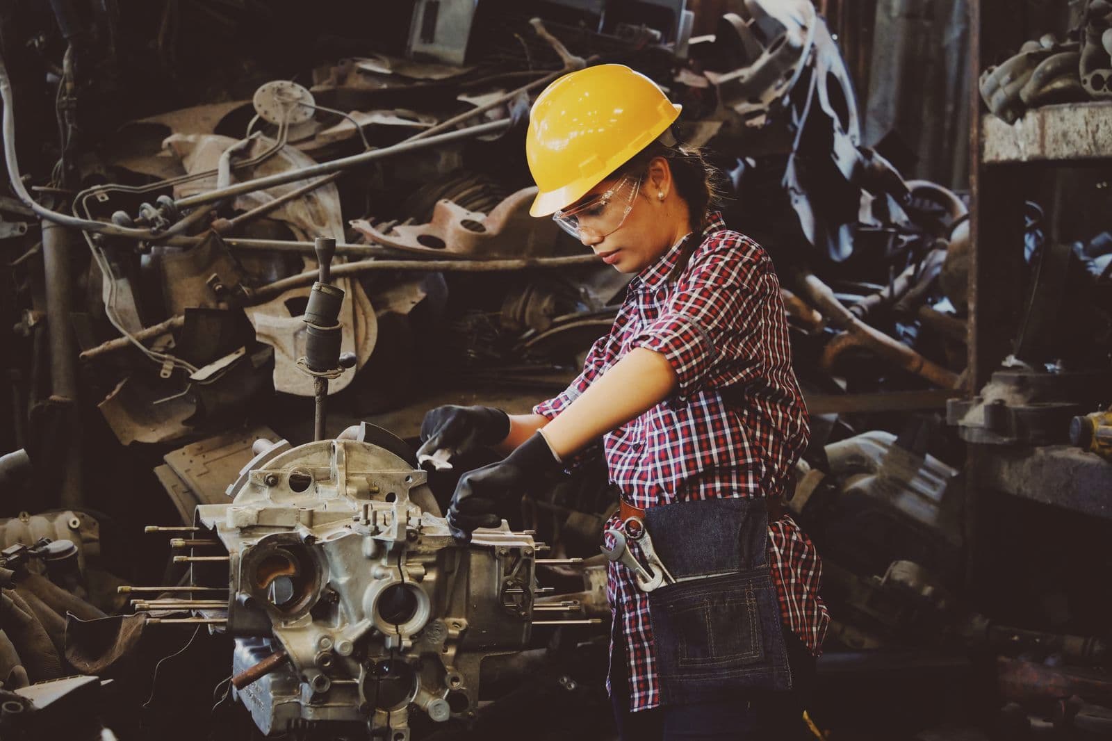 Une technicienne casquée intervient sur un moteur, dans un atelier.