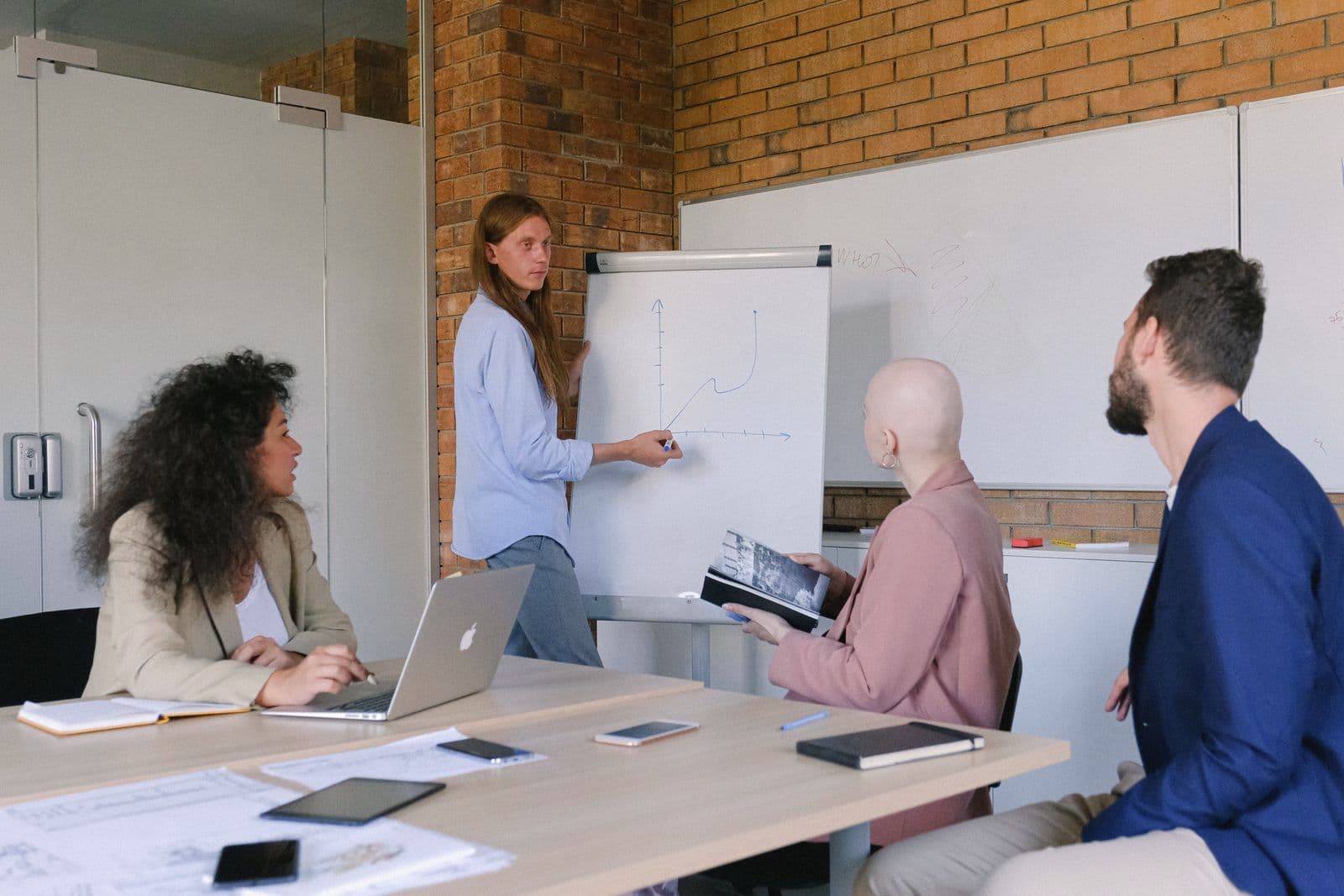 Une cheffe d'entreprise présente un tableau à ses collaborateurs, en réunion.