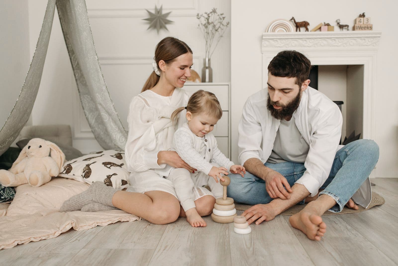Des parents jouent avec leur petite fille assis sur le parquet du salon.