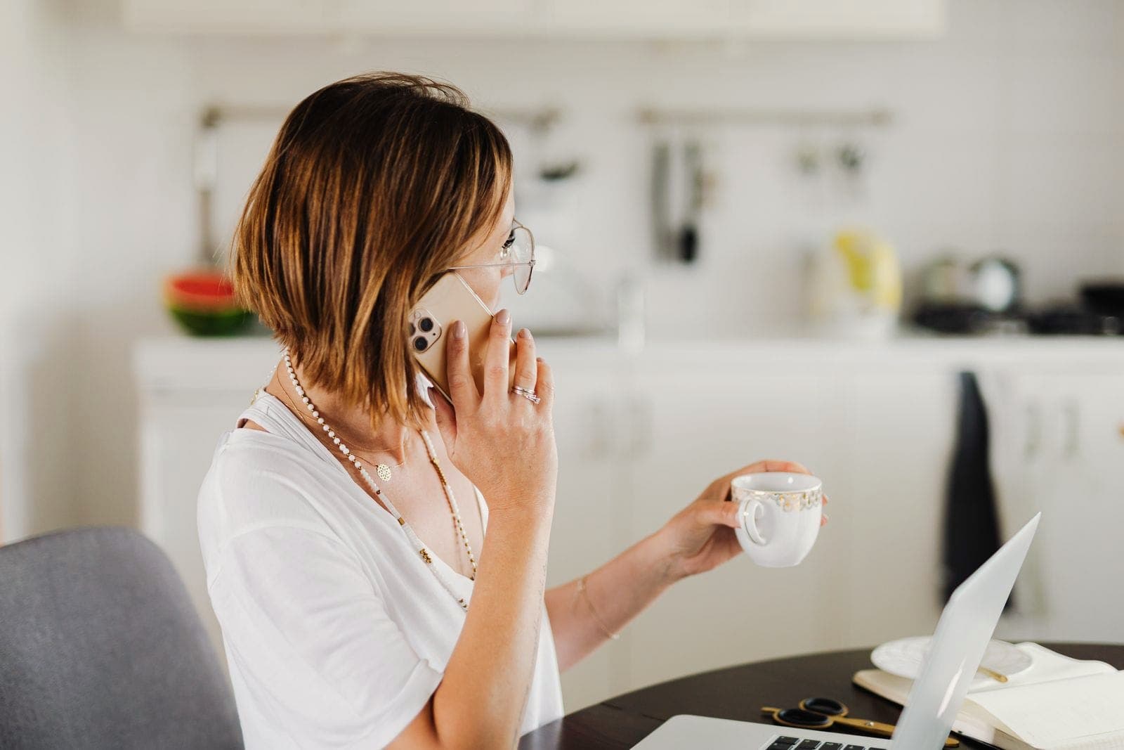 Une femme téléphone chez elle, une tasse de café à la main.