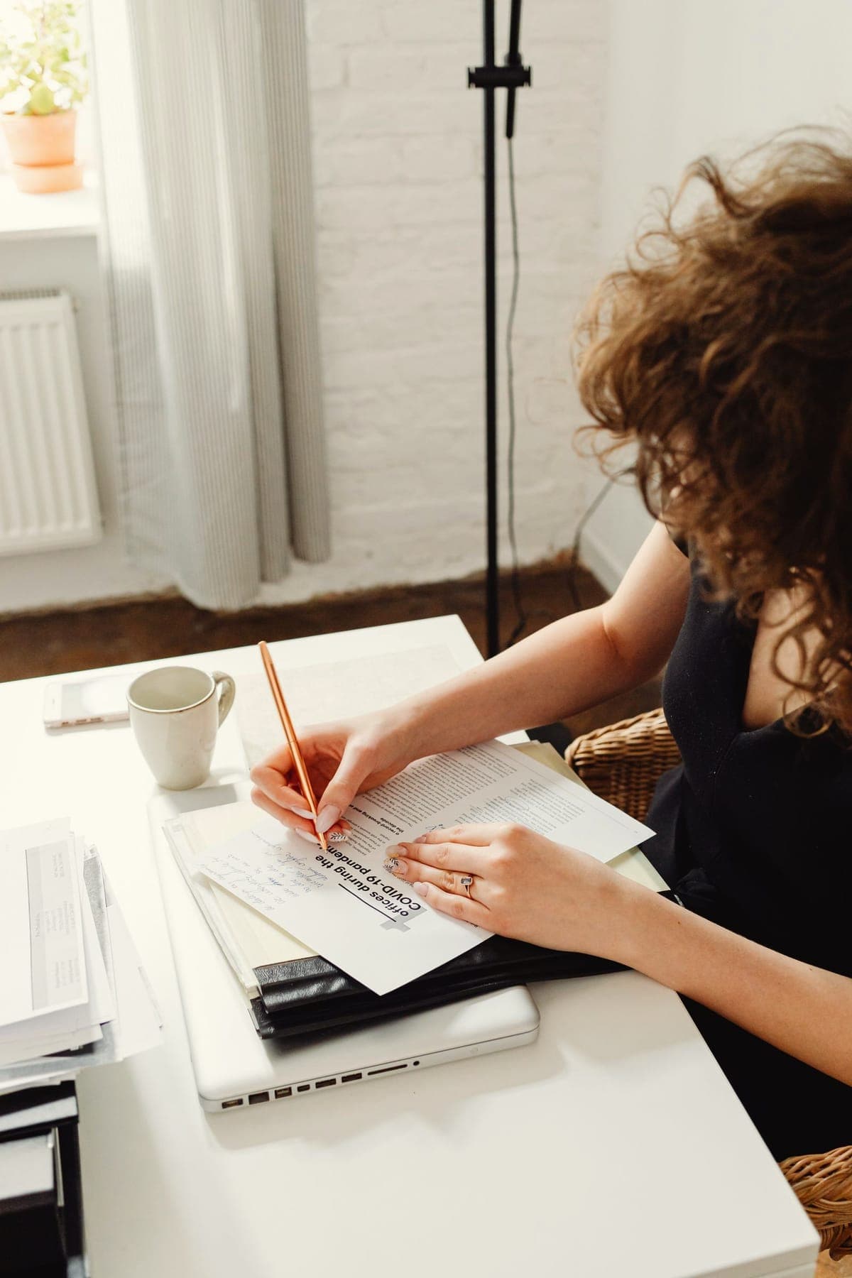 Une femme prend des notes à son bureau, entourée de documents.