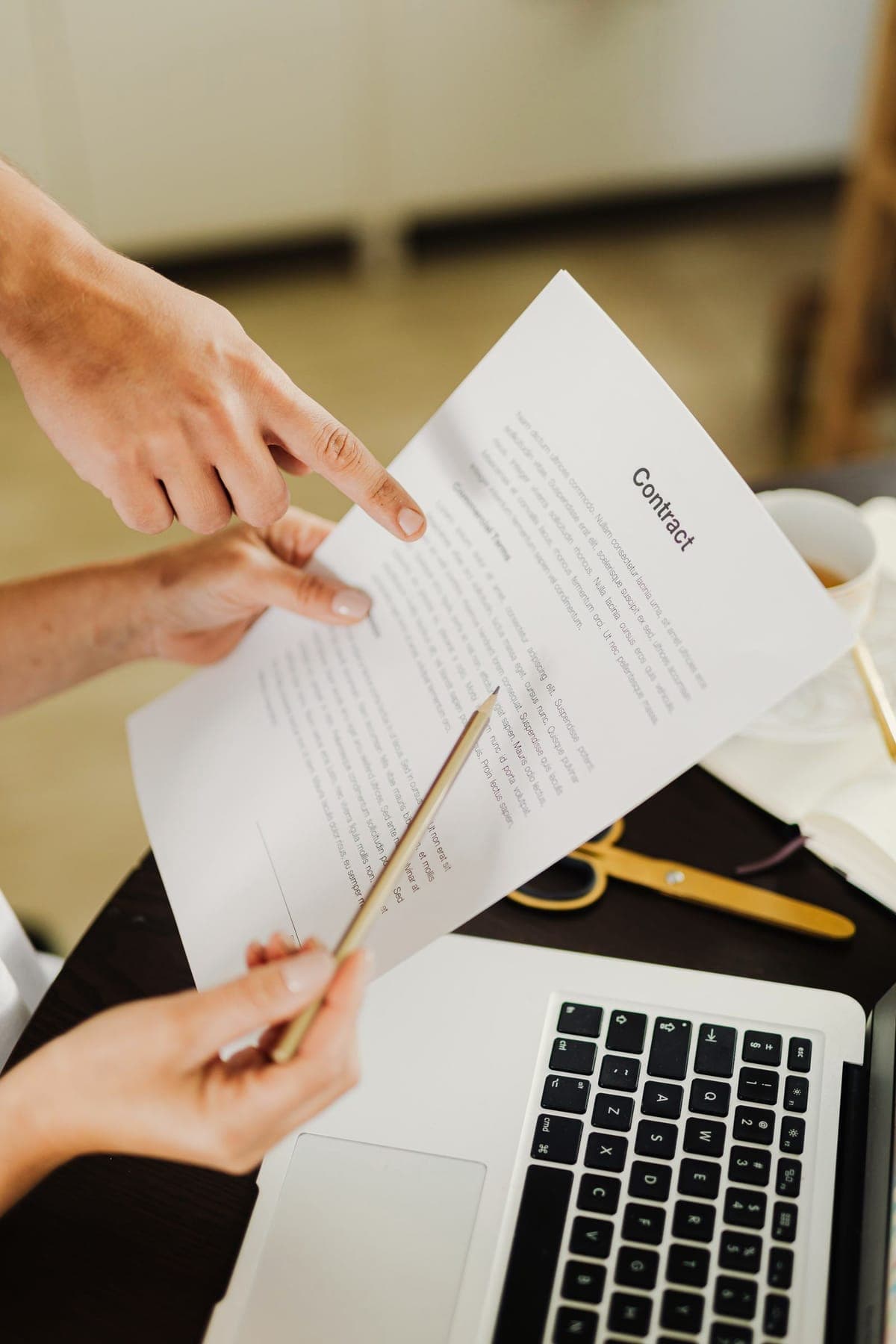Une main pointe un passage d'un contrat posé sur un bureau, près d'un ordinateur portable.