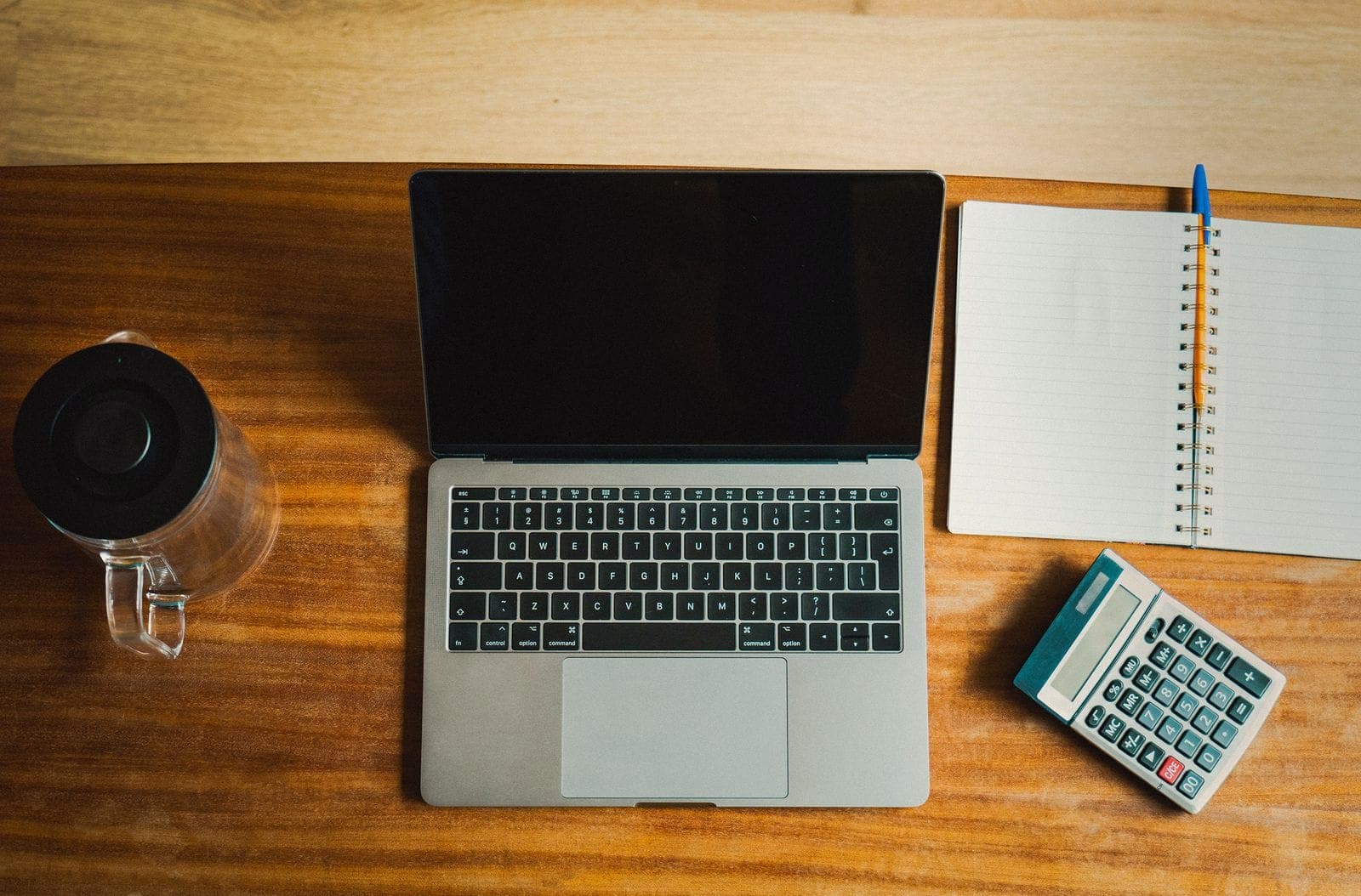 Vu de dessus, un bureau en bois avec un ordinateur portable, une calculatrice et un carnet.