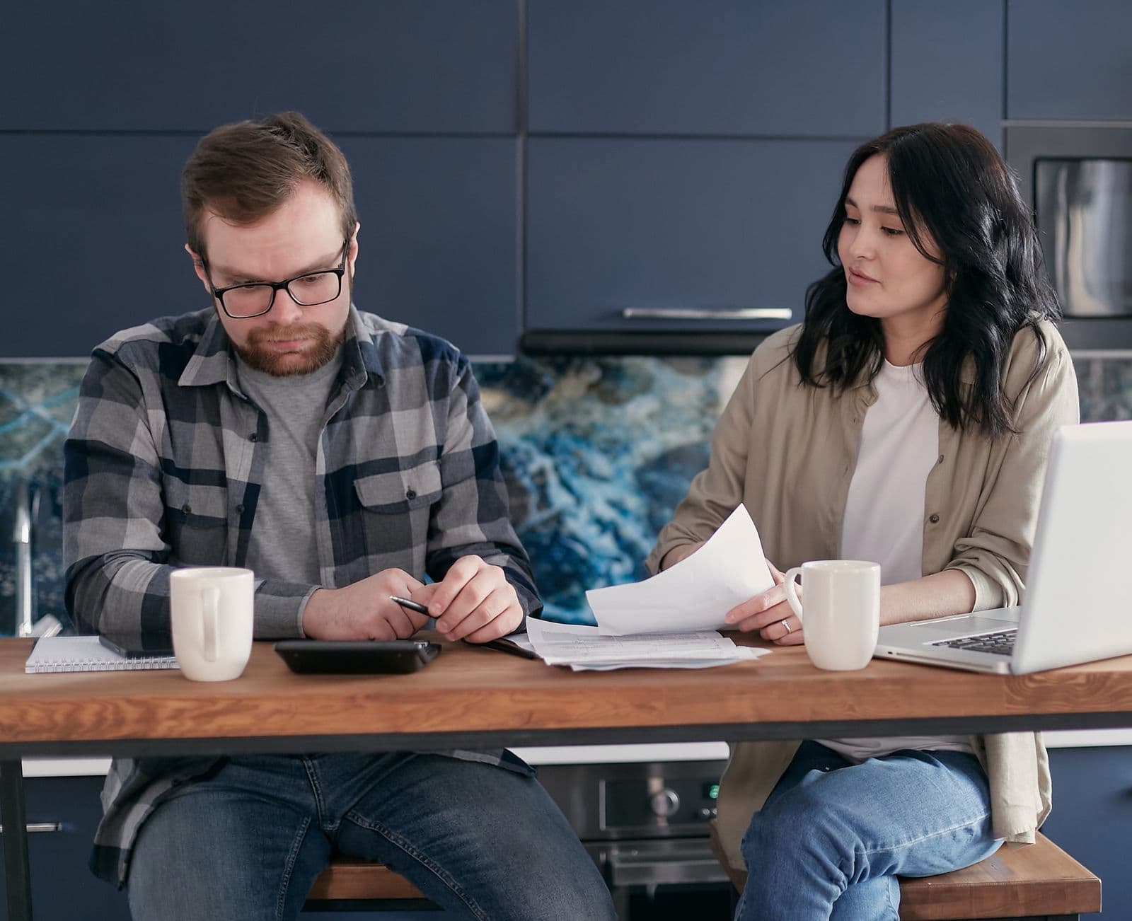 Un couple passe en revue ses papiers et ses comptes à la table de la cuisine, un ordinateur portable ouvert.