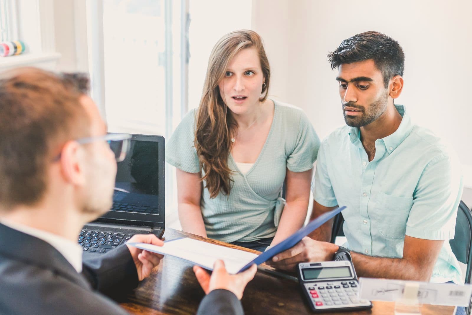 Un couple échange avec un conseiller, vu de dos, autour d'une table où sont posés des documents et une calculatrice.