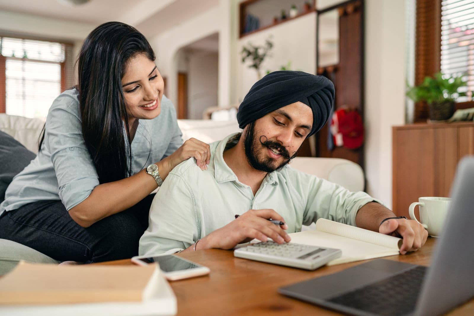 Un jeune couple fait ses comptes à table, avec une calculatrice et un ordinateur portable.