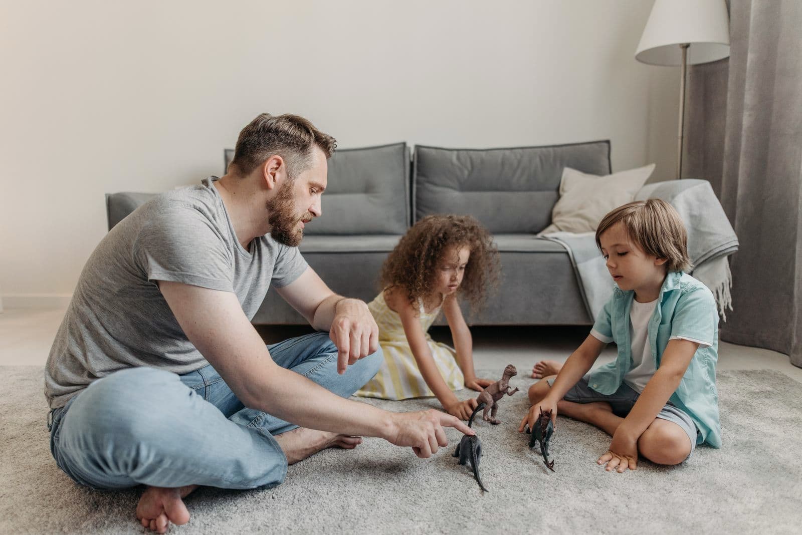 Un père joue avec ses deux enfants sur le tapis du salon.