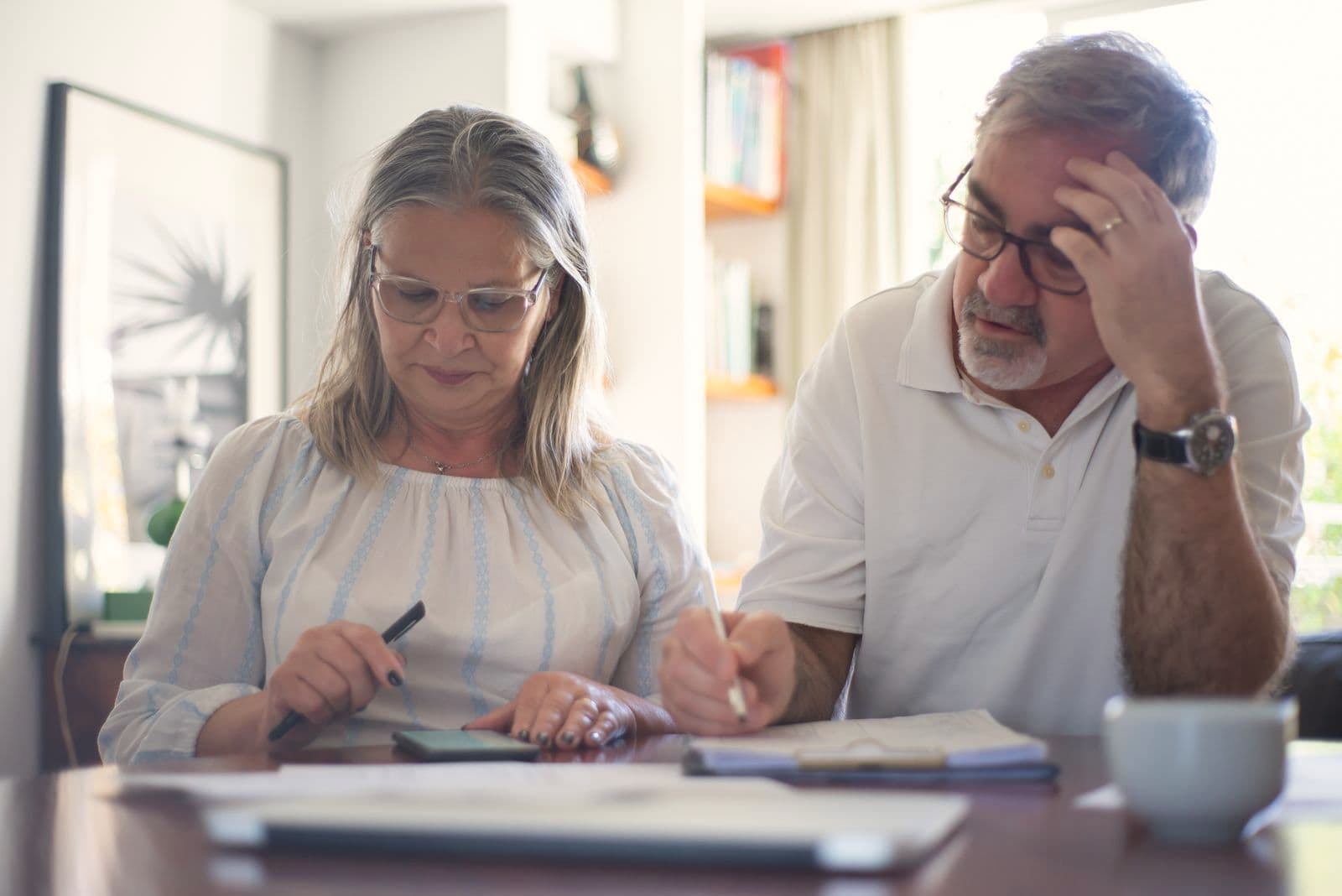 Un couple de retraités relit des papiers ensemble, à la table de son salon.