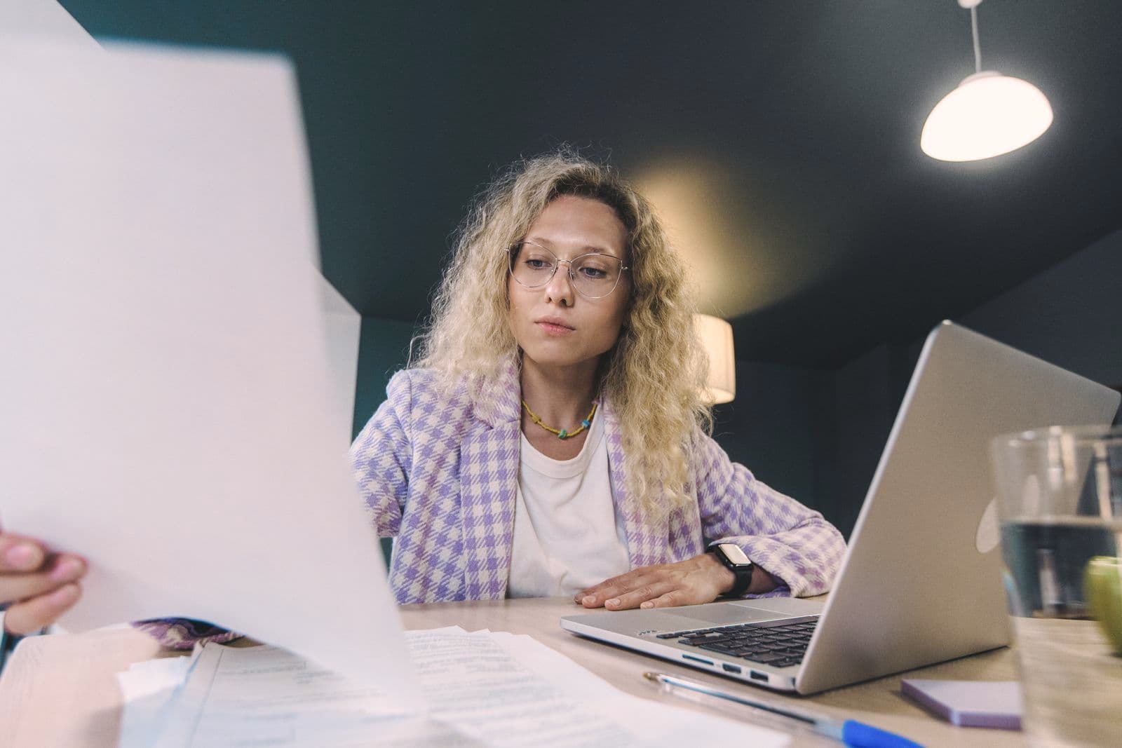 Une femme relit des documents devant son ordinateur portable, en fin de journée.